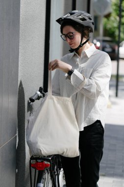 Eko çanta ya da pamuklu çanta taşıyan bir kadın şehirde bisiklet sürerken