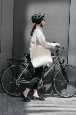 Eko çanta ya da pamuklu çanta taşıyan bir kadın şehirde bisiklet sürerken