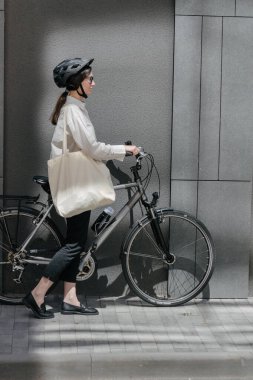 Eko çanta ya da pamuklu çanta taşıyan bir kadın şehirde bisiklet sürerken