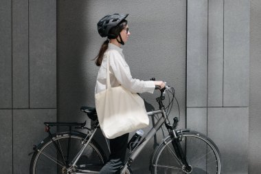 Eko çanta ya da pamuklu çanta taşıyan bir kadın şehirde bisiklet sürerken