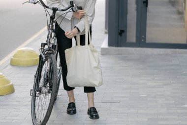 Eko çanta ya da pamuklu çanta taşıyan bir kadın şehirde bisiklet sürerken