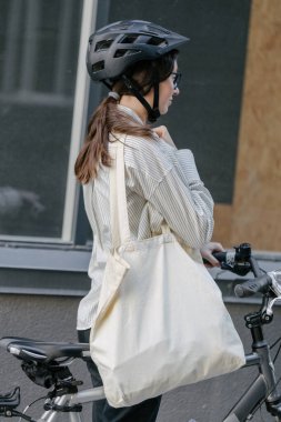 Eko çanta ya da pamuklu çanta taşıyan bir kadın şehirde bisiklet sürerken