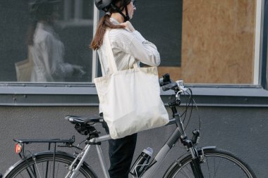 Eko çanta ya da pamuklu çanta taşıyan bir kadın şehirde bisiklet sürerken