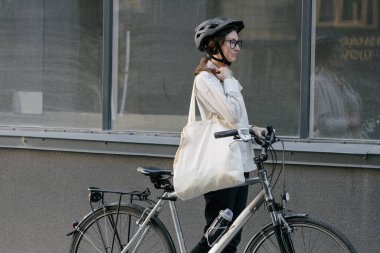 Eko çanta ya da pamuklu çanta taşıyan bir kadın şehirde bisiklet sürerken