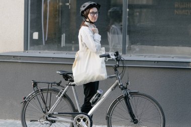 Eko çanta ya da pamuklu çanta taşıyan bir kadın şehirde bisiklet sürerken