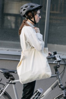 Eko çanta ya da pamuklu çanta taşıyan bir kadın şehirde bisiklet sürerken