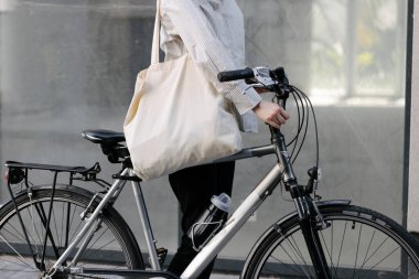 Eko çanta ya da pamuklu çanta taşıyan bir kadın şehirde bisiklet sürerken