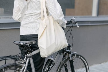 Eko çanta ya da pamuklu çanta taşıyan bir kadın şehirde bisiklet sürerken