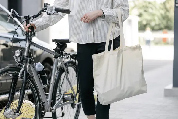 Eko çanta ya da pamuklu çanta taşıyan bir kadın şehirde bisiklet sürerken
