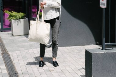 Beyaz çantalı bir kadın şehirde yürüyor.