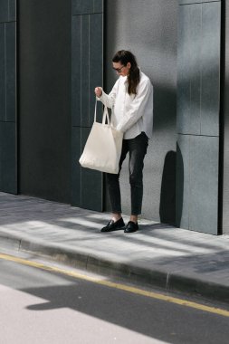Beyaz çantalı bir kadın şehirde yürüyor.
