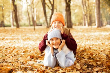 Sarı kuru yapraklarla dolu yerde, şirin şapkalı, gülümseyen kadın ve kız. Samimi sonbahar kıyafetleri içinde mutlu anne-kız eğleniyor ve Golden Park 'ta yürüyor. Her yerde ağaç yaprakları var..