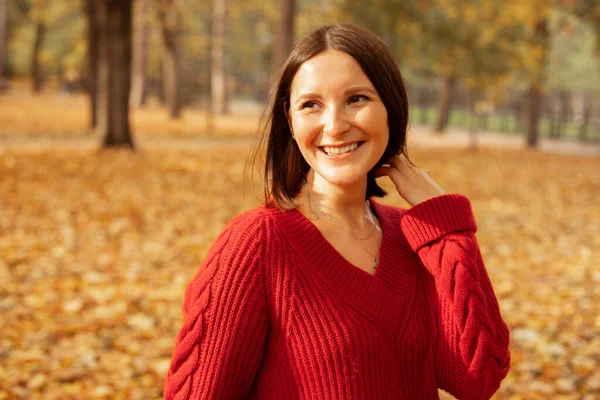 穿着舒适的红色针织毛衣 背景金黄 笑容可亲的迷人女人的画像 阳光明媚的日子 快乐的年轻女士在秋天的公园里散步 秋天的自然 积极的生活方式 户外休闲 — 图库照片