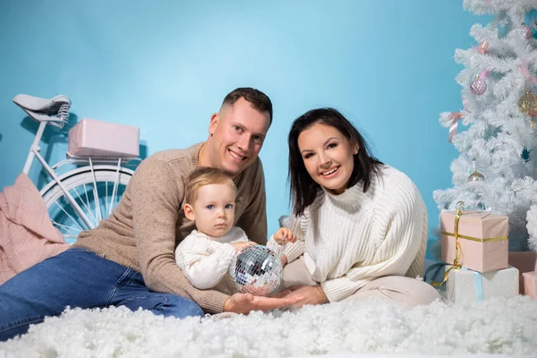 青色の背景に白い装飾とクリスマスの撮影場所に一緒に座って3人の家族の肖像画 幸せな母親 父と小さな息子はディスコボールで遊ぶ 年末年始 — ストック写真
