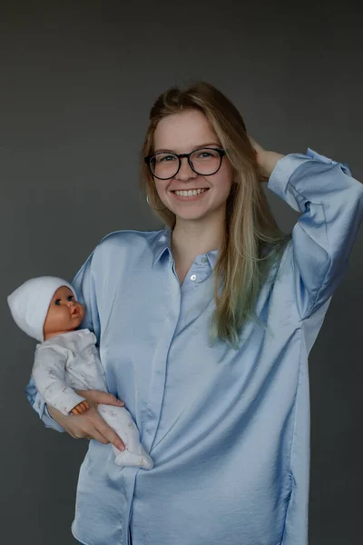 Happy future mother take birth preparation course, gray wall background, free copy space. Successful mastering of practical skills of newborns care. Training for pregnant women, practice on doll.