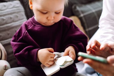 Kanepede oturan, elinde dijital termometreyle beyaz bir kutu tutan, akıllı telefondaki uygulamalara bilgi gönderen harika küçük kız çocuğunun portresi. Hemşire ev ziyaretleri, sağlık.