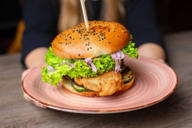 Restoranda tabağında şiş olan büyük, lezzetli bir hamburger. Sığır eti, kızarmış ekmekli domuz burger, siyah susam, sebze, pirzola ve pembe tabakta sos. Sağlıksız yemek ve suçluluk duygusu.