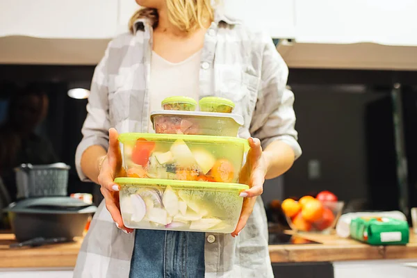 Hands of woman hold plastic containers with different frozen foodstuffs. Cooking dinner at home kitchen. Hermetically sealed food storage. Homemade dish, recipe, food ingredients and tableware.