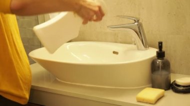 Banyo lavabosunun yüzeyine kadın el spreyi sıkıp süngerle ovala. Kadın ev hanımı tuvalette kirli mobilyaları temizliyor. Lavabo ve musluğu temizleyiciyle siliyorum. Temiz ev kavramı.