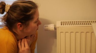 Donmuş kadın, loş ışık yakın çekim ile ana odadaki batarya ısıtma gücünü düzenliyor. Isıtma kaloriferinin yanında sıcak tut. Modern ev aletleri. Kapalı alanda düşük sıcaklık. Kış, soğuk, ısıtmasız..