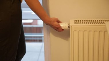 Kadın el, ana odada loş ışık ve yakınlaştırma kamerasıyla batarya ısıtma gücünü düzenliyor. Isıtma radyatörünü kapat. Modern ev aletleri. Kapalı alanda düşük sıcaklık. Kış, soğuk, ısıtmasız..