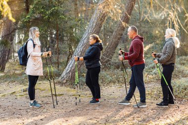 Ciddi kadın antrenör, bir grup insanla spor eğitmeni İskandinav usulü İskandinav yürüyüşleri öğretiyor, ormanda sopalarla yürüme egzersizleri, doğa. Takım arkadaşları için yürüyüş eğitimi alıyormuş. Sağlıklı yaşam biçimi