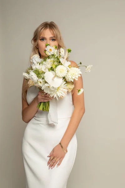 垂直自信を持って 魅力的でロマンチックなブロンドの女性の花嫁は スタジオでカメラを見て フィールドの花の花束で覆われた白いエレガントなドレスで 婚約と結婚の概念 スペースのコピー — ストック写真