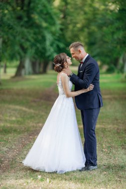 Yazın parkın dışında bekleyen neşeli çiftin yan görüntüsü. Genç damat, kollarını genç ve çarpıcı bir kadının boynuna koyuyor. Sarılıyor, gözleri görüyor, öpüşüyor. İlişki, aşk.