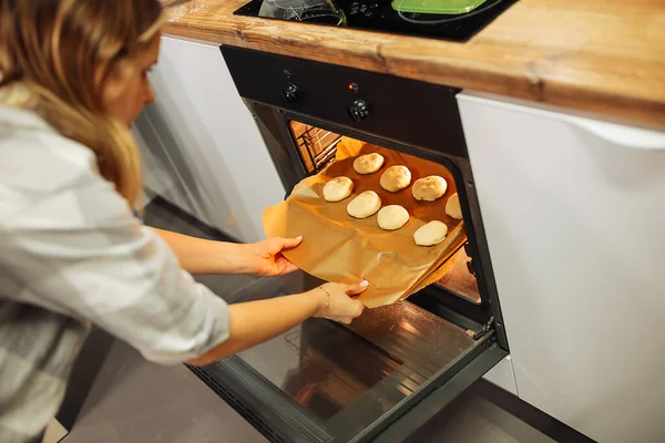 Woman put in preheated electric cooker tray with flour cakes on parchment paper. Baking cookies in oven at home kitchen. Homemade dessert, cooking recipe, delicious traditional pastry.