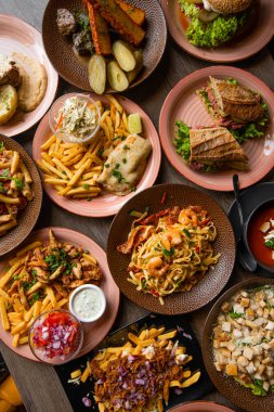 Kafe masasında çeşitli yiyecekler var. Sarımsaklı kraker, sandviç, patates kızartması etli patates, deniz ürünlü makarna, meyve ve sebze salatası ve tavuk yemeği.