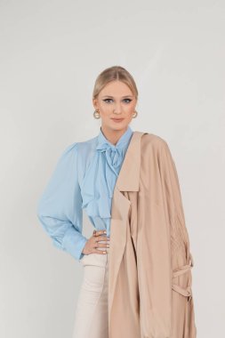 Portrait of graceful young woman in delicate blouse, cloak and pants, white background, free copy space. Business people, basic female clothes, casual office outfit, stylish seasonal look.
