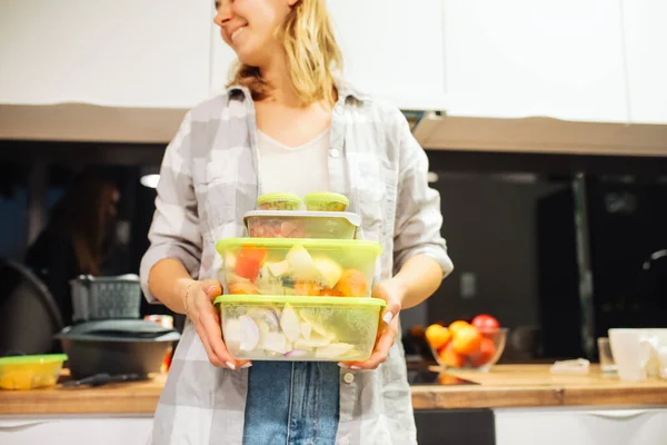 Happy woman hold plastic containers with different foodstuffs. Cooking dinner at home kitchen. Hermetically sealed food storage. Homemade dish, recipe, food ingredients and tableware.