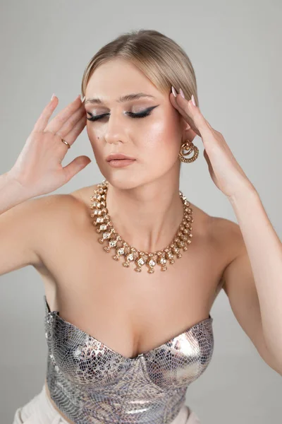 Woman with closed eyes in sexy top with open neckline, luxury necklace and evening makeup, white background. Exquisite female wear and jewelry for holidays. Celebration, formal event, festive look.