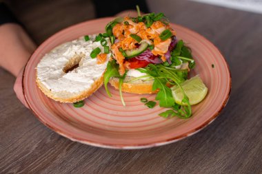 Closeup plate with delicious salmon burger isolated on wooden table background. Serving of healthy sandwich for breakfast. Fast food cafe, nutrition without meat, restaurant dish, meal.