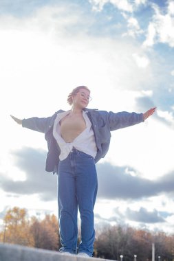 Vertical calm. satisfied, spiritual woman in jeans outfit stand on border with raised arms like in Titanic against cloudy and sunny sky horizon. Freedom and careless, feel free, i believe i can fly