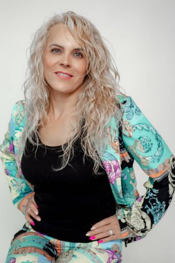 Gorgeous mature business woman with voluminous curly hairstyle in stylish turquoise pantsuit isolated on white background, copy space. Vintage female clothes, casual office outfit, lifting makeup.