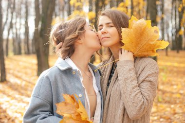 Nice, lovely family of mother and daughter having fun together, kissing and hugging on vacation, collect leaves and relax in golden woodlands. Family weekend in forest or park in autumn season
