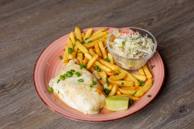 Close-up of pink ceramic plate with French fries, omelette, piece of lime, cabbage salad in small glass bowl sprinkled with greens on wooden table. Cooking, junk food, restaurant, menu, advertisement.
