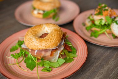 Side view of pink ceramic plate with fresh delicious burgers with hole in bun, bacon, arugula on wooden table. Cooking, restaurant, menu, advertising, fast food, junk food, cafe. Selective focus.