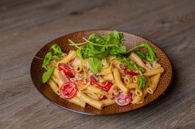 Close-up of palatable pasta with cherry tomatoes, arugula rucola and cheese served on brown round plate on wooden table. Cooking, advertisement, Italian cuisine, healthy food, restaurant, cookbook.