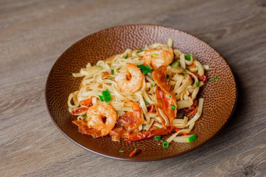 Top view of yummy pasta with shrimps, greens, pepper on brown beautiful plate on wooden table. Cooking, restaurant menu, advertising, cuisine, celebration, seafood, Italian cuisine, promotional.