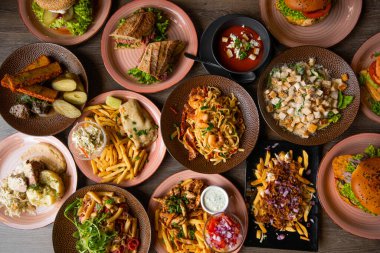 Top view of excellent food on table in cafe. Pasta with shrimps. Caesar salad with croutons. Sandwiches with lettuce. Pickled cucumbers, cheese sticks. Tomato soup. French fries, omelette. Burgers.