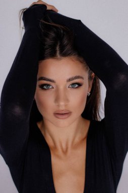 Beautiful sexy woman seductively touching hair with raised hands. Female portrait closeup. Gorgeous brown haired woman with passion posing in studio in black bodysuit. Feminine expressive look.