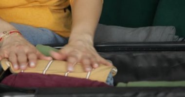 Video of unrecognizable woman hands stacking and folding clothes to travelling suitcase on wheels on sofa. Travel vacation preparation, migration to new place. Relocation, moving new apartment