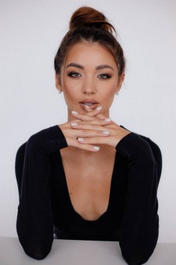 Cinsel kadın elleriyle dudağa dokunuyor. Beyaz arkaplan, kadın stüdyo portresi. Çekici kahverengi saçlı, yakasında siyah bir elbise olan bir model. Moda, kadınlık, güzellik.