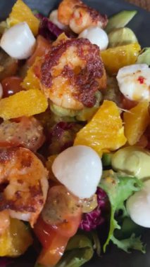 Seramik tabakta taze salata, ızgara karides, mozzarella peyniri, taze salata, sos, vişneli domates ve portakal dilimleri. İştah açıcı, davetkar Foof. 4k görüntü, dikey