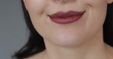 Unrecognizable woman shows lower part of her face. Emphasis is on snow-white teeth perfectly made by dentist. Professional makeup and . Concept of beauty. Studio grey background. 4k footage.