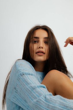 Büyük mavi kazaklı güzel kahverengi saçlı kadın. Beyaz arkaplan, kadın stüdyo portresi. Mükemmel makyajlı genç bir kadın günlük kıyafetlerle poz veriyor. Moda, tarz, temel kıyafetler..