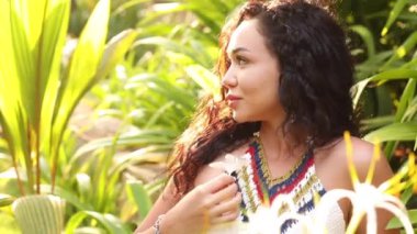 Olumlu duygular. Uzun dalgalı saçlı mutlu bir kadın lüks oteldeki tropikal bitki örtüsü arasında güzel bir bahçenin tadını çıkarıyor. Turizm ve seyahat. Adalardaki oteller. Egzotik cennet. Tam HD görüntüler.