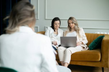 Bir grup iş kadını proje üzerinde çalışıyor, ikisi koltukta oturuyor, biri dizüstü bilgisayara hamile. İşletme ve girişimcilik. Rahat ve olumlu. Dost canlısı kadınlar takımı.. 